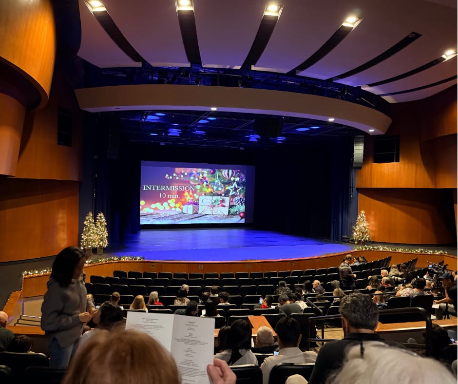 It is intermission time at a dance recital. Stage is empty, except for a slide indicating a ten minute intermission