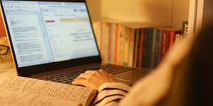 laptop screen (blurry) with some books and papers on the desk surrounding it