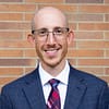 man wearing glasses and a tie smiles warmly