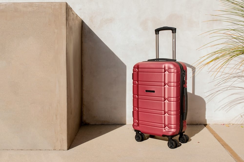 Red rolling bag suitcase against a wall