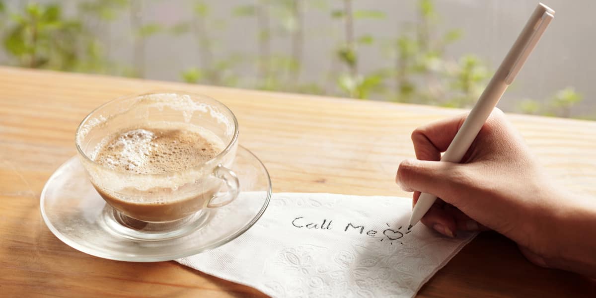 Coffee cup on a desk with a folded napkin with someone writing on it