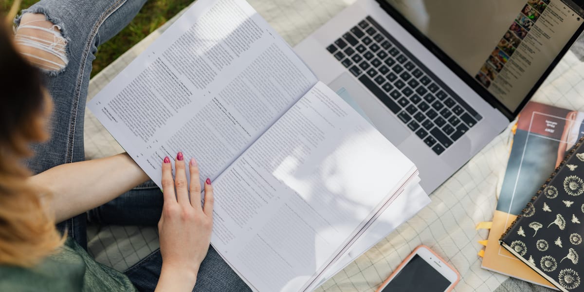 Student uses a laptop and has a textbook on their lap