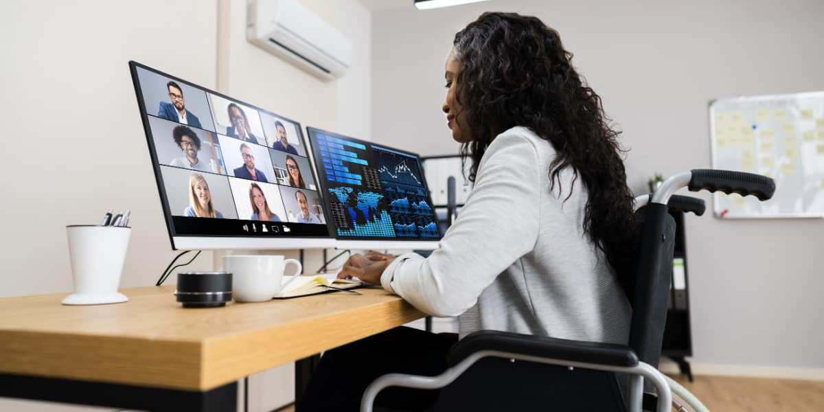 woman using a wheelchair sits at a desk with multiple monitors on it