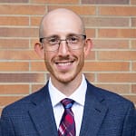 man wearing glasses and a tie smiles warmly