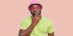 Man looking cheeky wearing a pink hat and pink heart-shaped sunglasses
