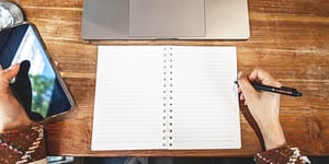 person prepares to write on a notepad with a laptop nearby