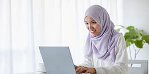 woman wearing a head scarf looks at her laptop