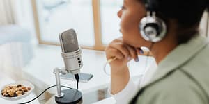woman talks into a podcasting microphone with some nuts as snacks off to the side on the table