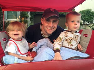 two kids in a wagon with their dad poking his head out between them