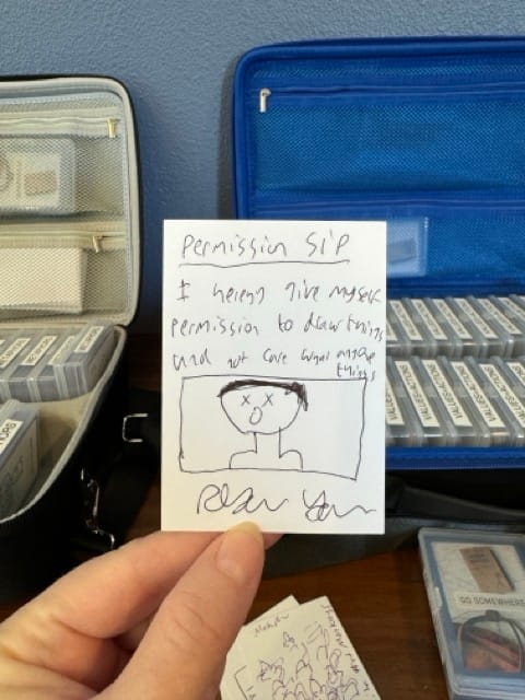 Person holds card that says: "I give myself permission to draw something and not care what anyone thinks." with a hand drawn self-portrait