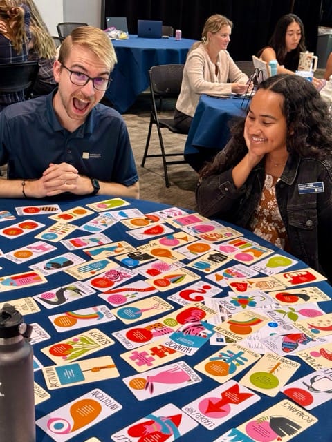 Two people pose in front of a table full of cards with values written on them. Words like: Loyalty Family Courage Curiosity Intellect