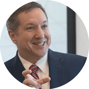 Man wearing a tie and jacket gestures while presenting at a conference