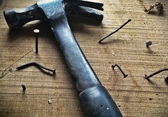 Hammer sits on a workbench with a lot of nails surrounding it (some of them bent)