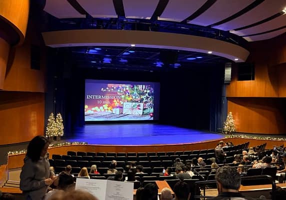 It is intermission time at a dance recital. Stage is empty, except for a slide indicating a ten minute intermission
